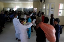 FILE - Afghan health workers measure the temperature of Afghan refugees to screen for coronavirus as they enter Afghanistan at the Islam Qala border crossing with Iran, in the western Herat Province, March 18, 2020.
