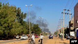 Des personnes déplacées par le conflit au Soudan marchent le long d'une route tandis que de la fumée s'élève au loin lors d'affrontements à Wad Madani, la capitale de l'État d'al-Jazirah, le 16 décembre 2023.