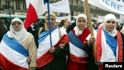 Perempuan Muslim yang mengenakan bendera Perancis berbaris di Paris saar protes undang-undang baru yang melarang simbol-simbol agama di sekolah-sekolah negeri Prancis, 14 Februari 2004. (Foto: Reuters)