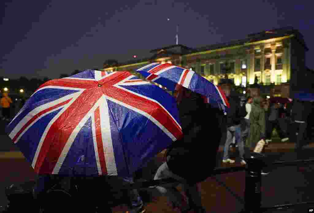 Two people walk with Union flag umbrellas as they stand in front of Buckingham Palace, after the announcement of the death of Queen Elizabeth II, in London, Sept. 8, 2022.