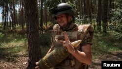 Військовик 14-тої окремої механізованої бригади імені князя Романа Великого тримає 155-мм снаряд неподалік лінії фронту на Харківщині, 19 липня 2023. REUTERS/Sofiia Gatilova