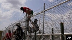 Migrantes que cruzaron el Río Grande desde México hacia Estados Unidos trepan una valla con alambre de púas, el lunes 21 de agosto de 2023, en Eagle Pass, Texas.