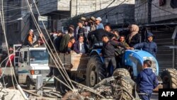 14일 가자지구 라파에서 사람들이 트랙터를 타고 건물 잔해 옆을 지나가고 있다.