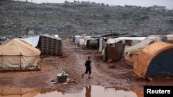 Seorang anak laki-laki asal Suriah tampak berjalan melalui area berlumpur di dekat tenda-tenda di kamp Kafr Arouk di Idlib, Suriah, pada 20 Desember 2021. (Foto: Reuters/Khalil Ashawi)