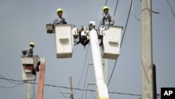 ARCHIVO - Obreros reparan cables eléctricos dañados por el huracán María en la comunidad Cantera en San Juan, Puerto Rico, el 19 de octubre del 2017. Actualmente la isla sufre de apagones crónicos en medio de advertencias de calor excesivo.
