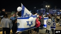 Personas con banderas de Israel reaccionan con entusiasmo cuando un vehículo que transporta a rehenes liberados por Hamás pasa hacia la base militar de Ofakim, en el sur de Israel, el 26 de noviembre de 2023.