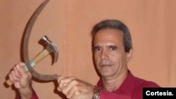 Jorge Fernández Era, escritor cubano, posa en su casa de La Habana, Cuba con una hoz y un martillo en una franca alusión al símbolo del comunismo, en una imagen para un post satírico en Facebook. [Foto cortesía del entrevistado].