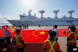 资料照：斯里兰卡港口工人在中国一带一路项目汉班托塔港手持中国国旗欢迎一艘中国考察船到港。（2022年8月16日）