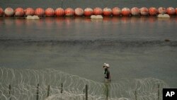 ARCHIVO - Un migrante de Columbia camina a lo largo de alambre y una barrera de boyas flotantes después de cruzar el Río Grande desde México hacia Estados Unidos, el lunes 21 de agosto de 2023, en Eagle Pass, Texas.