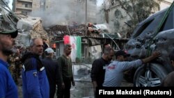 Personas llegan a la zona afectada y ayudan a remover un vehículo destruido, tras un ataque aéreo israelí contra el consulado de Irán en la capital siria, Damasco, el 1 de abril de 2024.
