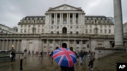 Seorang pengunjung dengan payung bermotif bendera Inggris berdiri di depan gedung bank sentral, Bank of England, di London, 3 November 2022. Bank of England akan menerapkan prosedur kepailitan kepada anak perusahaan Silicon Valley Bank di Inggris. (Foto: Kin Cheung/AP Photo)