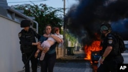 Agentes da polícia evacuam uma mulher e uma criança de um local atingido por um foguete disparado da Faixa de Gaza, em Ashkelon, no sul de Israel, a 7 de outubro de 2023.