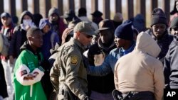 A member of US Customs and Border Protection tries to control a group of migrants as hundreds gather along the border after breaking through gaps in the border wall Dec. 5, 2023, in Lukeville, Ariz. 