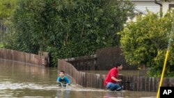 Un niño y un hombre andan en bicicleta a través de las inundaciones en Watsonville, California, el sábado 11 de marzo de 2023. (Foto AP/Nic Coury)