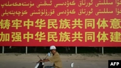 一名骑电摩托的男子路过新疆喀什莎车县的一面政府竖立的宣传牌。(2023年7月17日)