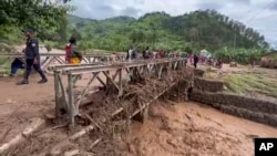 Watu wakivuka daraja lilifunikwa na kifusi cha mafuriko huko magharibi ya Rwanda Mei 3, 2023.
