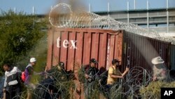 Un funcionario del Departamento de Seguridad Pública de Texas, a la derecha, observa mientras los migrantes caminan cerca de un vagón cubierto de alambre de Concertina en la frontera entre Texas y México, el miércoles 3 de enero de 2024, en Eagle Pass, Texas, EEUU.