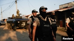 ARCHIVO - Oficiales de policía caminan delante de un vehículo militar blindado mientras participan en una operación conjunta militar y policial en el barrio Socio Vivienda, en Guayaquil, Ecuador, 26 de marzo de 2024.