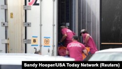 Workers in morgue operations shirts load body bags into a refrigerated trailer at Maui County Forensics Facility in Wailuku, Hawaii, Aug. 15, 2023. 