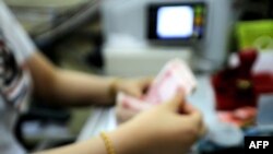 资料图片:这张摄于2015年8月11日的照片显示,在中国东部江苏省连云港的一家银行,一名出纳员正在清点人民币钞票。(法新社)