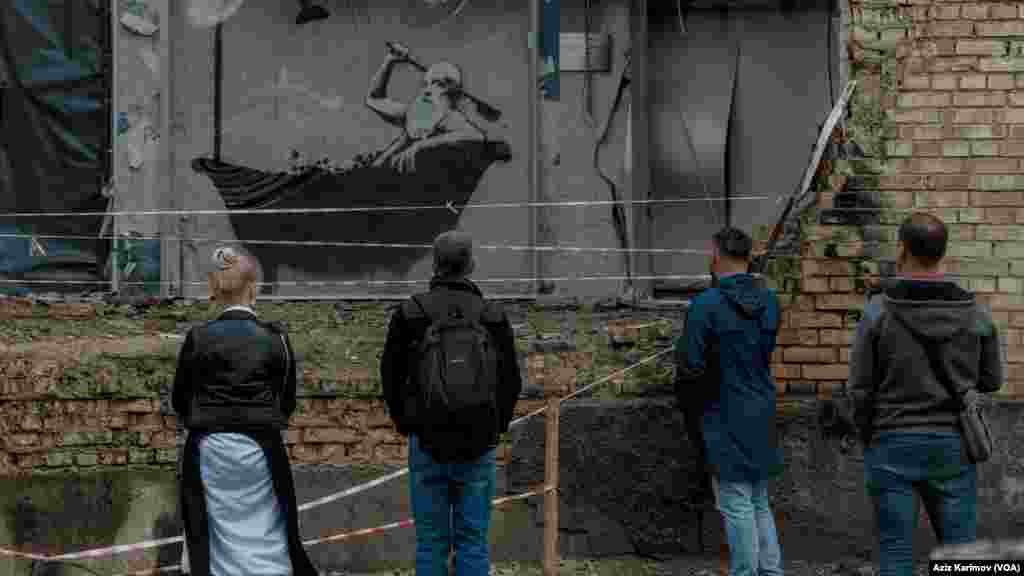Rusiya ordusunun atdığı bomba ilə dağıdılmış yaşayış binasının divarında britaniyalı rəssam Benksinin çəkdiyi əsəri izləməyə gəlmiş insanlar. Borodyanka, Xarkiv vilayəti, Ukrayna. 