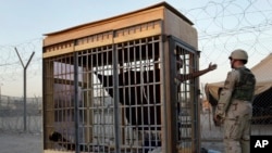 FILE - A detainee in an outdoor solitary confinement cell talks with a military police officer at the Abu Ghraib Prison on the outskirts of Baghdad, Iraq, June 22, 2004.
