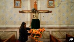 Una mujer adorna una imagen religiosa con flores de caléndula mexicana en la iglesia del cementerio municipal de Arocutin Michoacán, el domingo 31 de octubre de 2021.