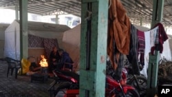 FILE - Syrian refugees warm themselves by a fire in front of tents set up in a public market space as shelter in Islahiye District of Gaziantep, southern Turkey, Feb. 11, 2023.