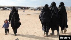 FILE - A woman holds a child's hand in the al-Hol camp, Syria, Jan. 8, 2020.