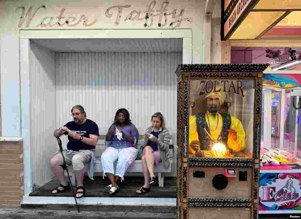 Visitantes del paseo marítimo disfrutan de un helado sentados junto a Zoltar, el adivino, una máquina que funciona con monedas que se hizo famosa en la película "Big", de Tom Hanks, mientras comienza el fin de semana festivo del Día del Trabajo en Rehoboth Beach, Delaware, EEUU.
