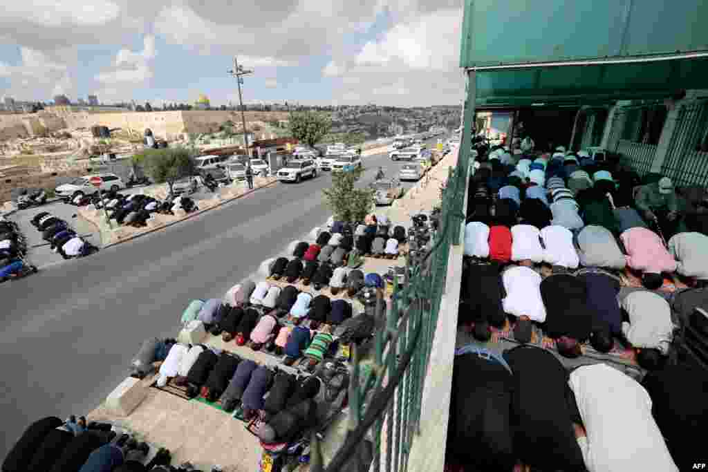 Muslim Palestinians take part in Friday Noon prayers in East Jerusalem neighborhood of Ras al-Amud, following age restrictions by Israeli security to above 50 years old for worshippers wanting to access the Al-Aqsa Mosque compound, top background, amid the ongoing battles between Israel and the Palestinian group Hamas. (Photo by AHMAD GHARABLI / AFP)