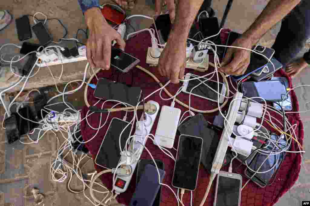 People sit by phone chargers connected to a communal group of electric socket hubs outside a closed pharmacy in Rafah in the southern Gaza Strip, amid ongoing battles between Israel and the Palestinian Hamas movement. (Photo by Mohammed ABED / AFP)