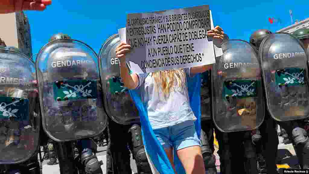 Una joven manifestante muestra un cartel delante de la barrera de seguridad de la Gendarmería Nacional.