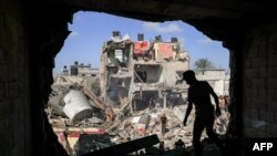 Seorang remaja berdiri depan lubang yang tadinya sebuah dinding pada sebuah bangunan yang dihantam roket Israel, di Khan Yunis, di selatan Jalur Gaza, 8 November 2023. (Foto: Mahmud Hams/ AFP)