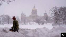 El edificio del Capitolio del Estado de Iowa es visible mientras Spud Glaser de Carlisle, Iowa, limpia la acera en el centro de Des Moines, Iowa, el martes 9 de enero de 2024, mientras una tormenta de nieve invernal azota el estado. (Foto AP/Andrew Harnik)