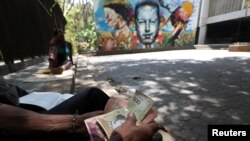 Un local cuenta notas de Bolívar venezolano frente a un mural que representa al difunto presidente venezolano Hugo Chávez en Caracas, Venezuela, 14 de marzo de 2019.