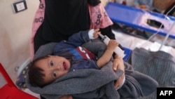 A woman holds her baby during treatment at a recently opened medical center for cholera cases in the Syrian town of Darkush, on the outskirts of the rebel-held northwestern province of Idlib, Oct. 22, 2022.