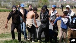 Para migran mengangkut seorang pria yang terluka dengan selimut dalam protes di Idomeni, Yunani (10/4). (AP/Amel Emric)