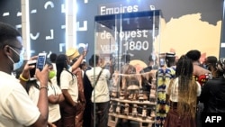 Des étudiants prennent des photos des artefacts pillés par les soldats coloniaux français retournés et exposés au grand public lors d'une exposition à la présidence à Cotonou, la capitale du Bénin, le 20 février 2022.
