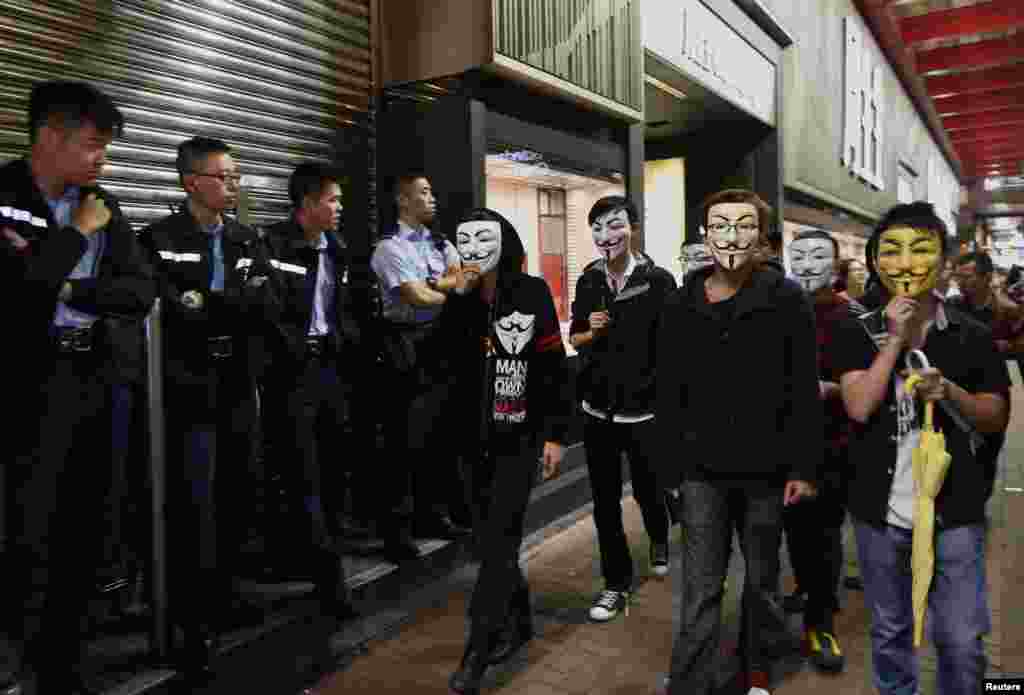 Demonstran pro-demokrasi mengenakan topeng "Guy Fawkes", berjalan melewati polisi di jalanan yang mereka kuasai sebagai bagian dari aksi gerakan sipil "Occupy Central" di distrik Mongkok, Hong Kong, 5 November 2014.