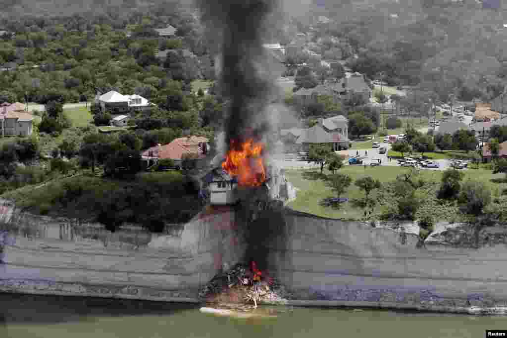 Asap membumbung dari sebuah rumah yang sengaja dibakar, beberapa hari setelah tanah di mana rumah itu berdiri longsor ke Danau Whitney, Texas. Petugas bangunan membakar rumah mewah di pinggir danau yang menggantung sekitar 75 kaki (23 meter) di tebing yang goyah tersebut. 