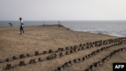 Des hommes s'étirent devant une installation artistique de l'artiste sénégalais Yakhya Ba, le long de la promenade maritime de Dakar, le 11 mai 2022.