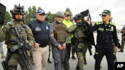 En esta foto publicada por la Oficina de Prensa de la Presidencia de Colombia aparece la escolta policial de Dairo Antonio Úsuga, centro, también conocido como "Otoniel", líder del violento cartel Clan del Golfo antes de su extradición a EEUU en un aeropuerto militar en Bogotá, Colombia, el miércoles 4 de mayo de 2022. (Oficina de Prensa de la Presidencia de Colombia via AP)