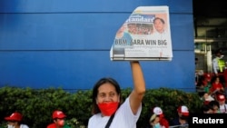 A supporter of presidential candidate Ferdinand ‘Bongbong’ Marcos Jr. holds up a newspaper with the winning of Marcos Jr. on the headline, as people gather to celebrate as partial results of the 2022 national elections show him with a wide lead over rivals.