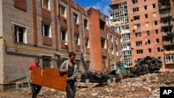 Two men carry a wooded panel next to heavily damaged buildings and destroyed cars in a Russian bombing in Bakhmut, eastern Ukraine, May 24, 2022.