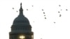 La silueta de un peatón temprano en la mañana contra el amanecer mientras camina frente a las banderas de EEUU en el National Mall y pasa por el edificio del Capitolio en Washington, el 7 de noviembre de 2022.