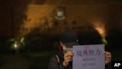 Una manifestante sostiene un cartel con los mensajes "Fuerzas extranjeras no, fuerzas internas" y "El abuso del poder del gobierno hunde a la gente en la miseria y el sufrimiento" durante un encuentro en la Universidad de Hong Kong, el martes 29 de noviembre de 2022. 