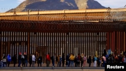 Migrantes hacen fila cerca de la valla fronteriza, después de cruzar el Río Bravo, para solicitar asilo en El Paso, Texas, EEUU, visto desde Ciudad Juárez, México, el 5 de enero de 2023.