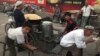 FILE - Uighurs rest near a food stall and Beijing Olympic Games billboards in Kashgar in China's western Xinjiang province, Aug. 30, 2016.