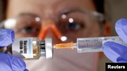 FILE - A woman holds a small bottle labeled "Vaccine COVID-19" and a medical syringe in this illustration taken April 10, 2020. 